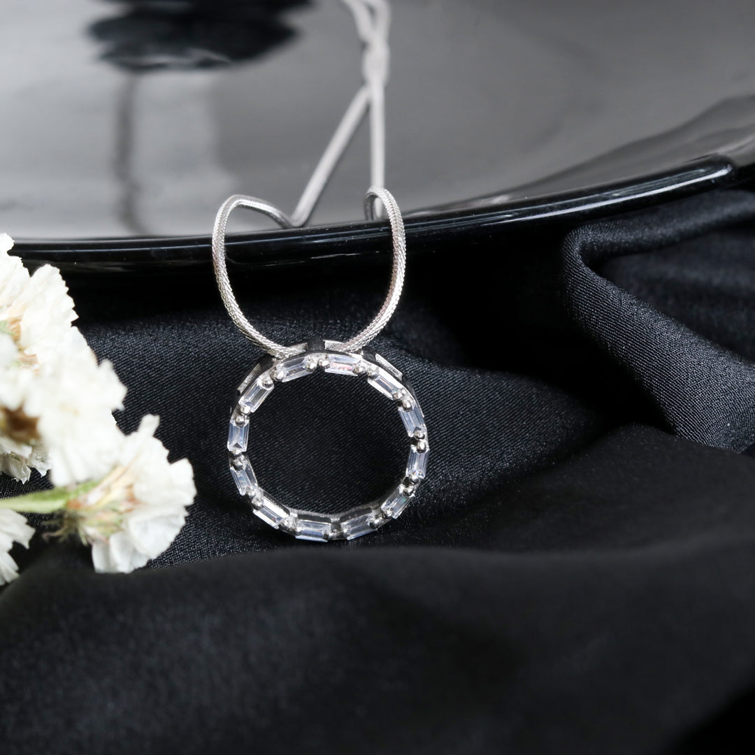 Silver necklace with a circular pendant on a black surface with white flowers.